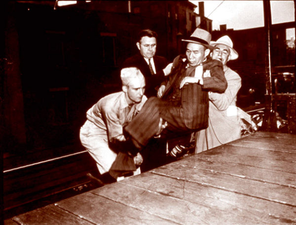 A soldier and two other men lift an elderly Japanese man onto the train platform for deportation, ca. 1943